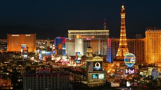 Bunt beleuchtete Silhouette von Las Vegas. Im Vordergrund ein Gebäude, das dem Pariser Eiffelturm nachempfunden ist.
