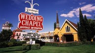 Auf einer grünen Wiese steht ein rotes Schild, auf dem 'Wedding Chapel' zu lesen ist, dahinter eine kleine gelbe Kapelle