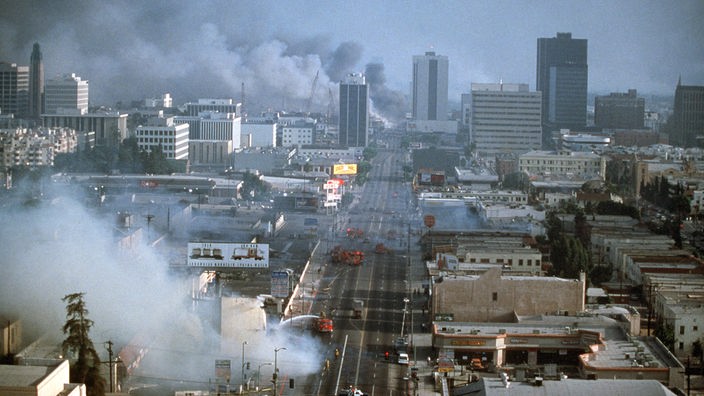 Stadtansicht von Los Angeles. Über der Stadt steigen mehrere Rauchsäulen auf.