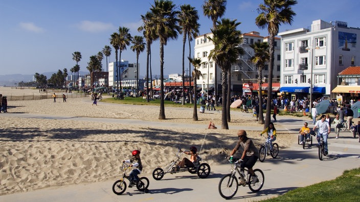 Palmen stehen am Strand von Venice Beach und auf der Promenade fahren viele Bewohner Fahrrad. | Bildquelle: Mauritius Palmen stehen am Strand von Venice Beach und auf der Promenade fahren viele Bewohner Fahrrad.