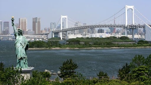 Blick auf eine Imitation der Freiheitsstatue und eine Hängebrücke. Im Hintergrund die Wolkenkratzer von Tokio.