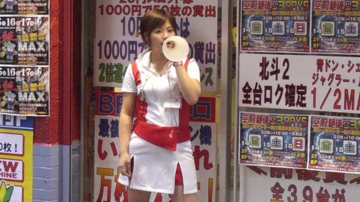 Ein Mädchen in rot-weißer Uniform mit kurzem Rock ruft durch ein Megaphon.