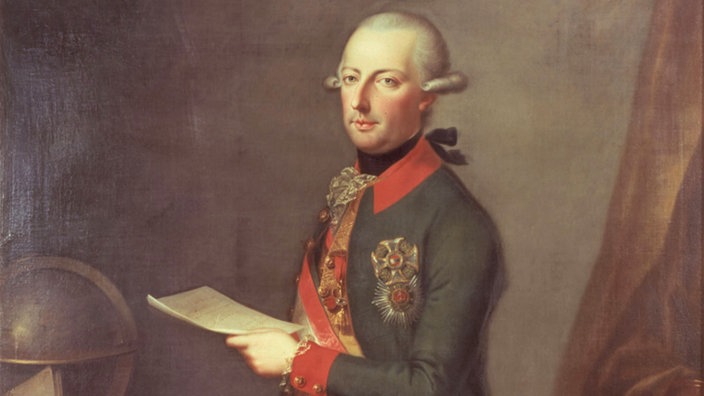 Kaiser Joseph II. in seiner kaiserlichen Tracht. Die Haare hat er der Mode nach zum Zopf gebunden. Er steht an seinem Schreibtisch, den ein Globus und eine Landkarte zieren. | Bildquelle: akg Kaiser Joseph II. in seiner kaiserlichen Tracht. Die Haare hat er der Mode nach zum Zopf gebunden. Er steht an seinem Schreibtisch, den ein Globus und eine Landkarte zieren.