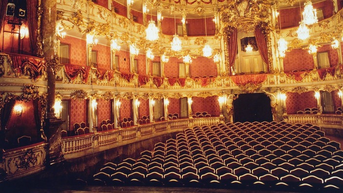 Der Rokoko-Saal des Cuvilliés-Theaters. Emporen über vier Stockwerke ermöglichen Besuchern eine gute Sicht. Sie sind mit Schnörkeln verziert und goldweiß lackiert. Eine edle Tapete ziert die Wände. Kronleuchter hängen von der hohen Decke und schaffen eine festliche Stimmung. | Bildquelle: wdr Der Rokoko-Saal des Cuvilliés-Theaters. Emporen über vier Stockwerke ermöglichen Besuchern eine gute Sicht. Sie sind mit Schnörkeln verziert und goldweiß lackiert. Eine edle Tapete ziert die Wände. Kronleuchter hängen von der hohen Decke und schaffen eine festliche Stimmung.