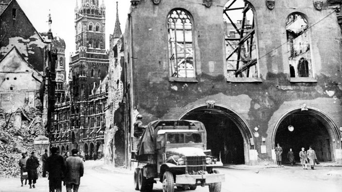 München nach Bombenangriffen im Zweiten Weltkrieg. Häuser und Kirchen sind stark beschädigt. Dächer, Wände und Fenster fehlen.