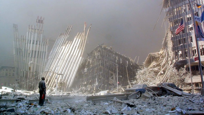 Ein Mann steht in einem riesigen Trümmerfeld, hinter ihm die Reste der Stahlkonstruktion der Twin Towers