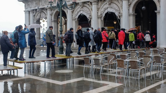 Menschen gehen auf einem Steg über einen überfluteten Platz | Bildquelle: Imago/Julien Mattia/Le Pictorium Menschen gehen auf einem Steg über einen überfluteten Platz