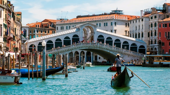 Die Rialtobrücke und der Canal Grande, im Vordergrund ein Gondoliere mit Gondel | Bildquelle: picture alliance / dieKLEINERT Die Rialtobrücke und der Canal Grande, im Vordergrund ein Gondoliere mit Gondel