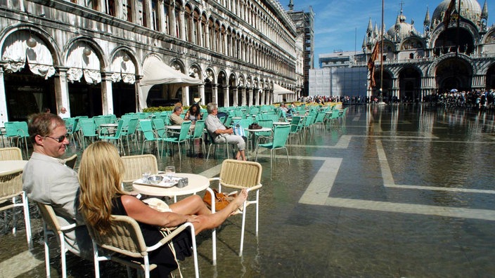 Touristen auf dem Markusplatz, Restaurantstühle stehen im Wasser | Bildquelle: dpa/Andrea Merola Touristen auf dem Markusplatz, Restaurantstühle stehen im Wasser