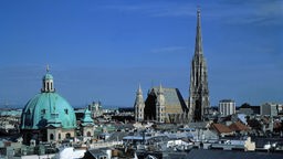 Stadtansicht von Wien: Vor blauem Himmel ist die Altstadt mit dem Stephansdom und der Karlskirche zu sehen. 