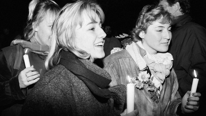 Die Schwarzweiß-Fotografie zeigt drei junge Frauen mit Kerzen in den Händen bei einer Demonstration.