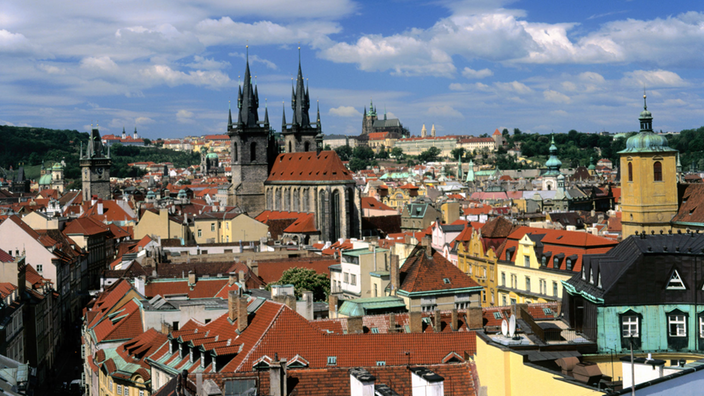 Zu sehen sind sonnenbeschienene Dächer der Prager Altstadt vor blauem Himmel.