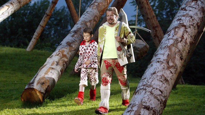 Foto von 2004: Tell-Schauspieler läuft mit Kind durch angedeuteten Wald.