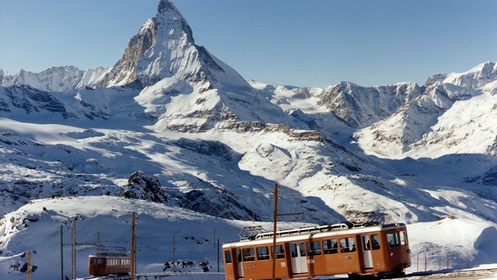 Eine rote Zahnradbahn fährt über ein Schneefeld, im Hintergrund das Matterhorn | Bildquelle: WDR/Andreas Kaster Eine rote Zahnradbahn fährt über ein Schneefeld, im Hintergrund das Matterhorn