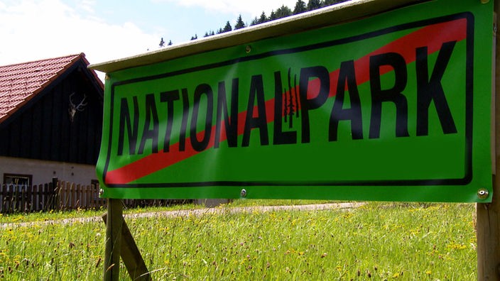 Protest: Ein grünes Plakat mit der Aufschrift 'Nationalpark', welche mit einem roten Balken durchgestrichen ist.