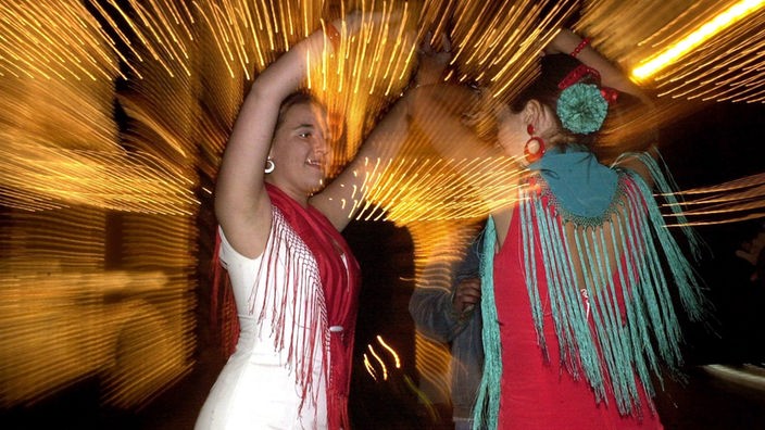 Zwei Frauen in traditionellen Flamenco-Kleidern tanzen in Sevilla in die Nacht hinein.