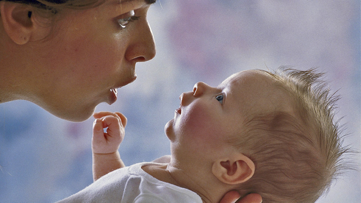 Eine Mutter hält ihren Säugling dicht vors Gesicht und spricht mit ihm.