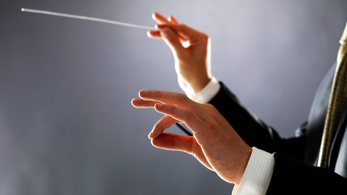Ein Mann dirigiert mit dem Taktstock in der Hand.