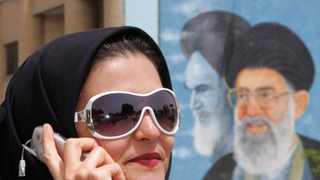 Eine iranische Frau mit Sonnebrille, Kopftuch und Handy.