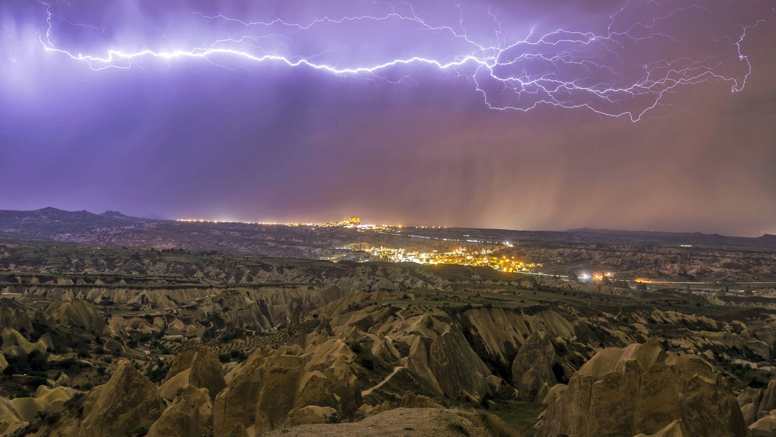 Blitze über der Felsenlandschaft von Kapadokien, im Hintergrund eine beleuchtete Stadt