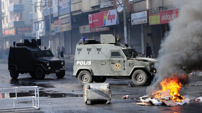 Brennende Barrikaden und gepanzerte Polizeifahrzeuge auf einer Straße