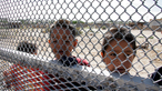 Zwei mexikanische Jungs schauen durch den engmaschigen Grenzzaun zwischen Mexiko und den USA.