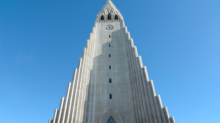 Ein hoher Kirchturm läuft in Bögen nach links und rechts in kleiner werdenden Säulen aus