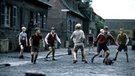 Szene aus dem Film Das Wunder von Bern: Auf dem matschigen Weg vor einigen Zechenhäusern spielen Jungen mit einem Lumpenball Fußball.