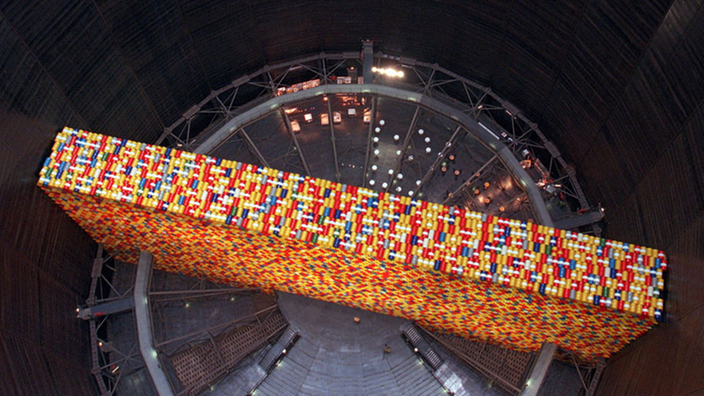 Blick von oben in das Innere des Gasometer Oberhausen. Das Bodenrondell wird diagonal von einer überdimensionalen Wand aus farbigen Fässern geteilt, die der Künstler Christo dort aufgestellt hatte.