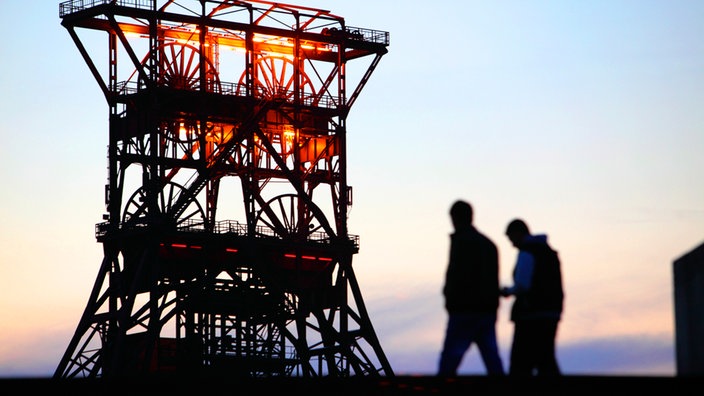 Zwei Arbeiter vor Förderturm des Gelsenkircheners Schachts Consolidation. | Bildquelle: Newspixx Zwei Arbeiter vor Förderturm des Gelsenkircheners Schachts Consolidation.