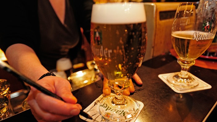 Kellnerin markiert Bierdeckel unter Pilsglas.