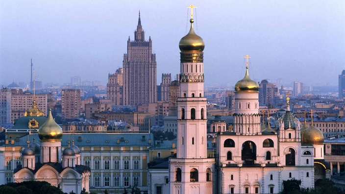 Stadtansicht von Moskau: im Vordergrund eine Kirche mit goldenen Zwiebeltürmen, im Hintergrund Hochhäuser.
