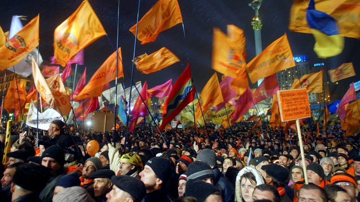 Menschenmenge bei Nacht mit orangefarbenen Fahnen.