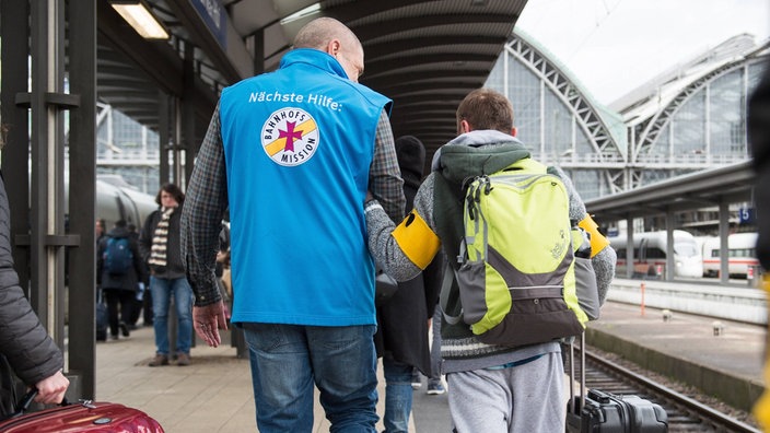 Ein Mitarbeiter der Bahnhofsmission begleitet einen sehbehinderten Fahrgast am Bahnsteig. | Bildquelle: imago images/brennweiteffm Ein Mitarbeiter der Bahnhofsmission begleitet einen sehbehinderten Fahrgast am Bahnsteig.