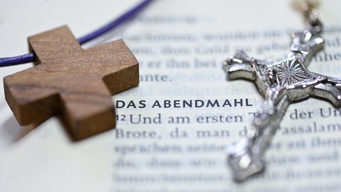 Ein Holzkreuz und ein Kruzifix neben dem Wort "Abendmahl" in einer Bibel | Bildquelle: picture alliance / epd-bild Ein Holzkreuz und ein Kruzifix neben dem Wort "Abendmahl" in einer Bibel