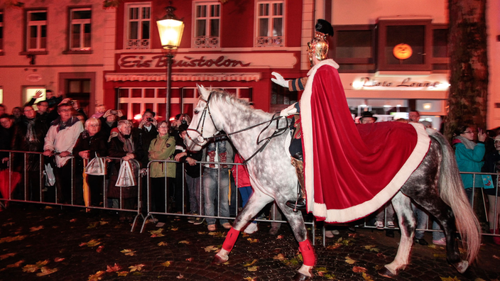 Sankt Martin bei einem Straßenumzug als römischer Offizier auf einem Pferd sitzend und mit einem roten Mantel bekleidet.