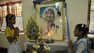 Zwei Mädchen beten vor einem Bild von Mutter Teresa