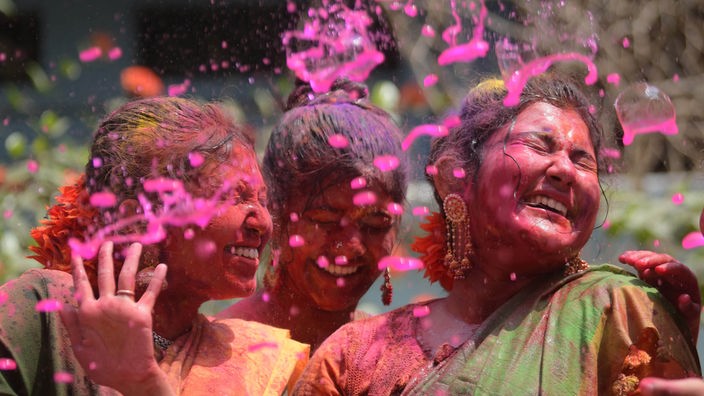 Drei lachende Frauen bewerfen sich mit Farbe