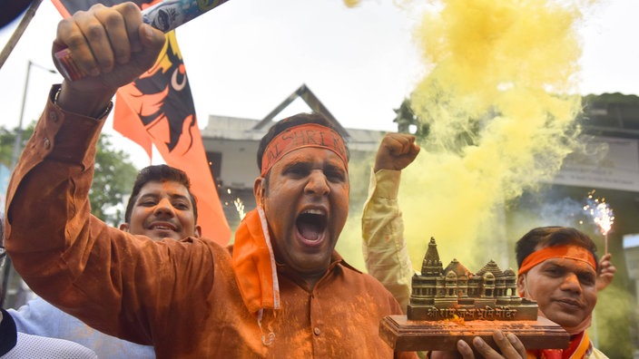 Ein schreiender Mann in Orange hält in einer Hand ein Tempel-Modell und in der anderen eine rauchende Fackel | Bildquelle: imago images/Hindustan Times Ein schreiender Mann in Orange hält in einer Hand ein Tempel-Modell und in der anderen eine rauchende Fackel