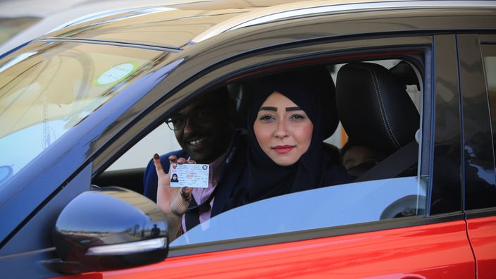 Eine saudische Frau sitzt am Steuer eines Autos und zeigt ihren Führerschein