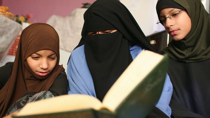 Drei junge Frauen lesen im Koran.