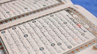 Bild eines aufgeschlagenen Korans in arabischer Schrift mit reichlich Verzierungen im Text.