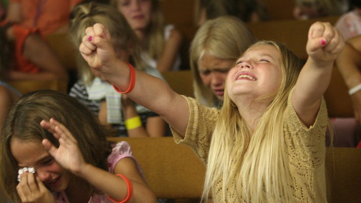 Drei Mädchen weinen und heben ihre Hände bei einer kirchlichen Veranstaltung in den USA