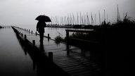 Eine Person mit Regenschirm geht über einen Bohlensteg am Meer