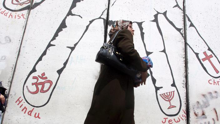 Eine palästinensische Frau läuft an einem religiösen Graffiti an einer Wand in Bethlehem vorbei | Bildquelle: dpa Eine palästinensische Frau läuft an einem religiösen Graffiti an einer Wand in Bethlehem vorbei