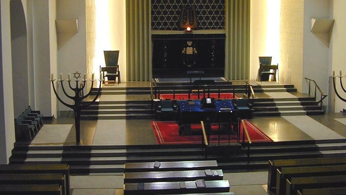 Innenraum einer Synagoge: Man sieht unter anderem Sitzbänke und einen siebenarmigen Leuchter.