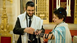 Rabbi legt einem Jungen den Gebetsriemen an