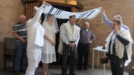 Jüdische Hochzeit: Das Brautpaar steht in einer Synagoge, zwei Männer halten ein großes Tuch über die beiden