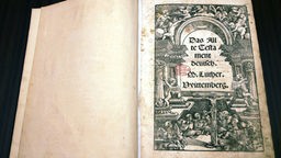 Auf einer Buchseite steht in verschnörkelter Schrift: 'Das Alte Testament, deutsch, M. Luther, Wittenberg'.