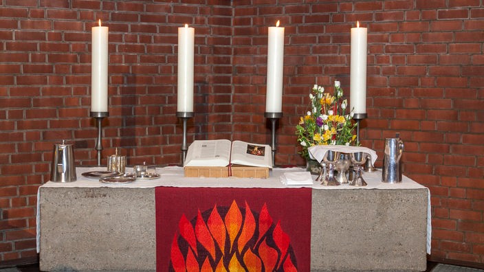 Für einen Konfirmationsgottesdienst ist der Altar vorbereitet: Kerzen brennen, die Bibel ist aufgeschlagen, das Geschirr für das Abendmahl steht bereit